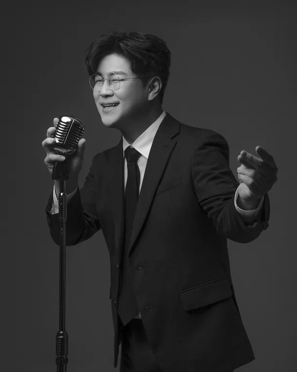 마이크 스탠드 앞에서 웃으며 노래하는 박구윤